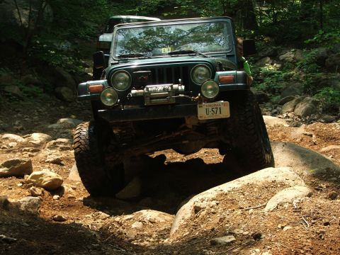 1996 Ford Bronco - A green Jeep Wrangler tackles a challenging rocky trail, with another vehicle visible in the background.