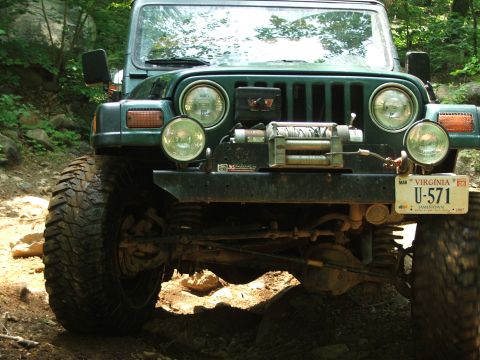 1996 Ford Bronco - Front view of a green Jeep Wrangler on an off-road trail, equipped with a winch.