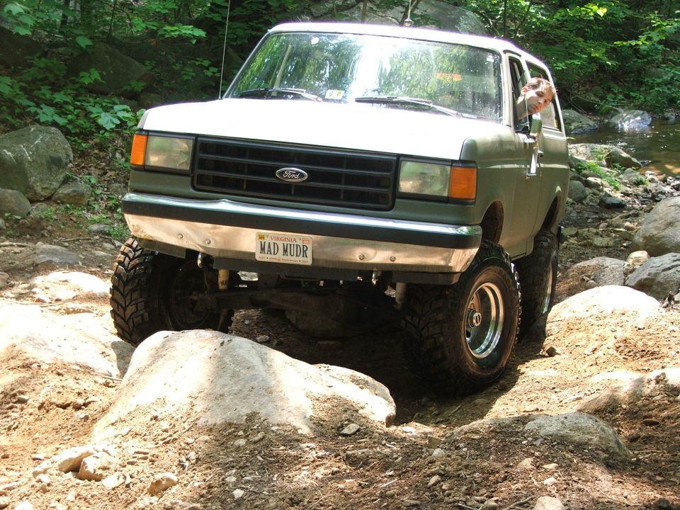 Green Ford Bronco with a "MAD MUDR" license plate navigating rocky terrain