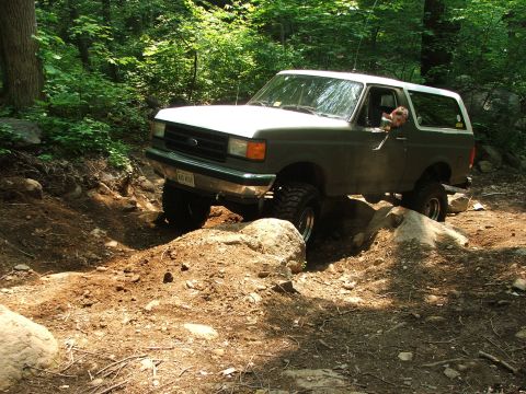 1996 Ford Bronco - A 1996 Ford Bronco tackles a challenging rocky path in a wooded area.