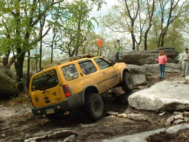 Yellow SUV navigating a rocky off-road trail with people watching