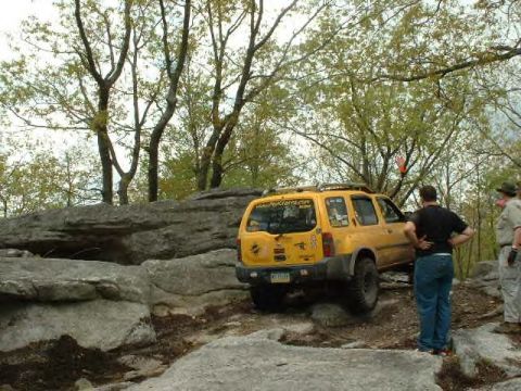 1991 Ford Bronco - A yellow SUV navigates a rocky trail with several people observing the off-road adventure.
