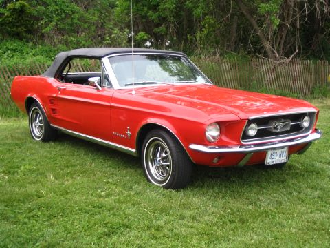 1993 Ford Taurus - A bright red 1967 Ford Mustang convertible sits on a grassy lawn, its black top up.