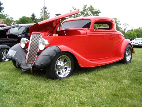 1993 Ford Taurus - A bright red coupe hot rod is displayed with its hood open at a car show, parked on a grassy field.