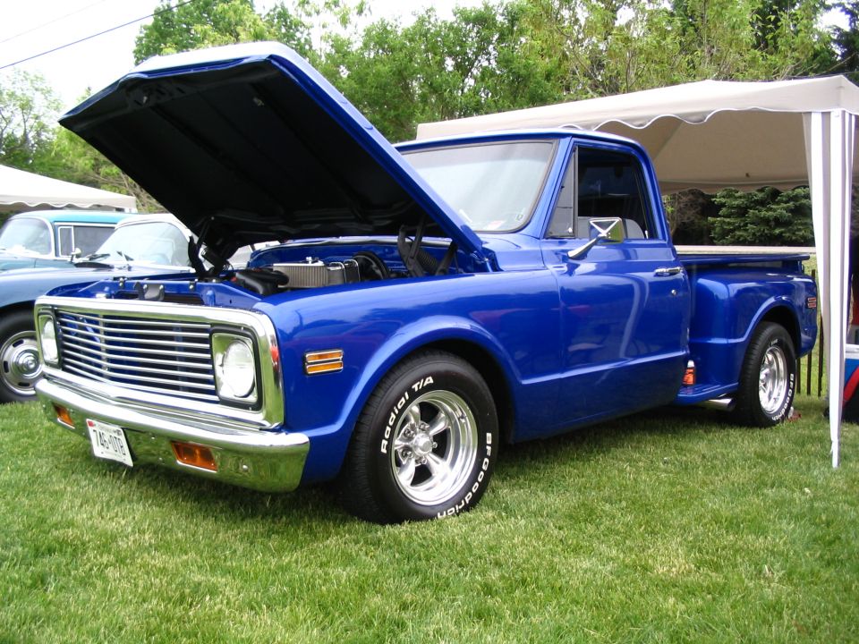 blue pickup truck with hood open, parked on grass next to a tent. Another vehicle is partially visible behind it