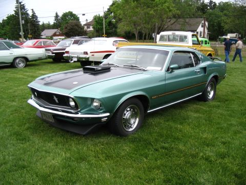 1993 Ford Taurus - A green 1969 Ford Mustang Mach 1 is parked on a grassy field with other vehicles in the background.