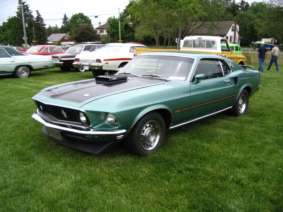 Green 1969 Ford Mustang Mach 1 with black hood scoop and stripe, parked on grass