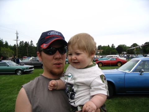 1993 Ford Taurus - Man and baby at a car show with multiple vehicles in the background.