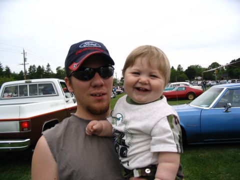 1993 Ford Taurus - A man and a baby pose for a photo at an outdoor car show with several vehicles visible in the background.