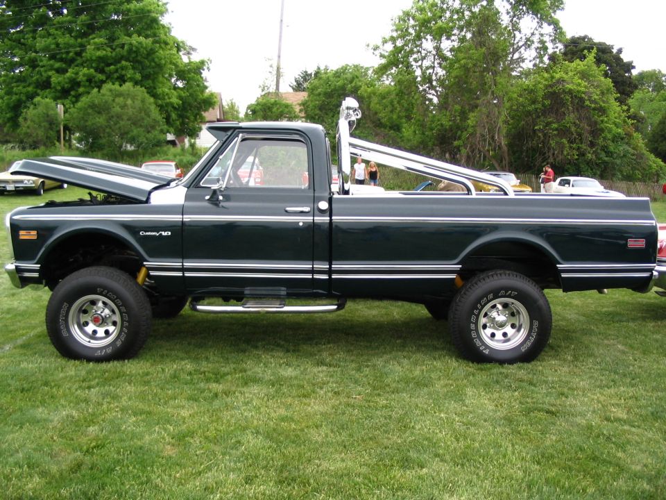 Side view of a dark green 1971 Chevrolet C10 pickup truck with a chrome roll bar and lifted suspension