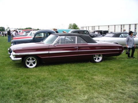 1993 Ford Taurus - Maroon 1963 Ford Galaxie convertible at a car show with other vehicles in the background.