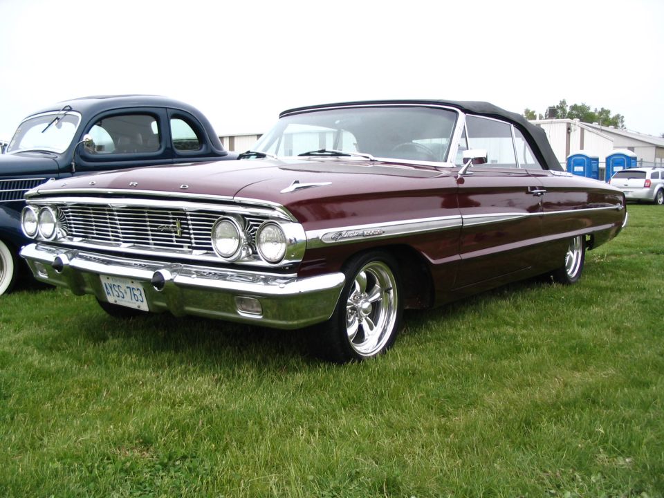 Maroon convertible with black top parked on grass next to a dark blue coupe