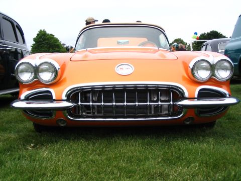 1993 Ford Taurus - A classic orange Chevrolet Corvette is parked on grass, with other vehicles in the background at an outdoor event.