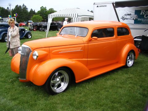 1993 Ford Taurus - A classic orange hot rod sedan is displayed at a car show with other vehicles in the background.