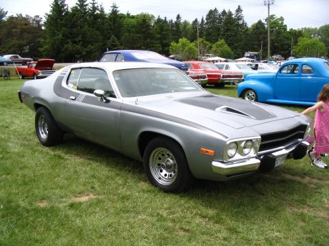 1993 Ford Taurus - A silver 1973 Plymouth Satellite Sebring is displayed at an outdoor car show with other vehicles in the background.