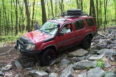 1991 Ford Bronco - This red SUV is equipped for off-road adventures, tackling a challenging rocky path in a wooded area.