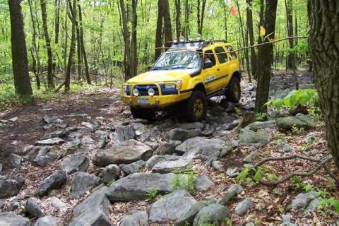 1991 Ford Bronco - A yellow SUV navigates a challenging rocky path through a dense forest.