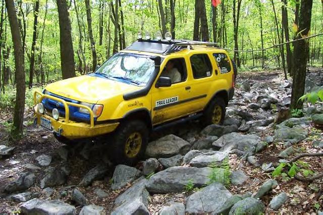 Yellow SUV with snorkel and roof rack navigating a rocky forest trail
