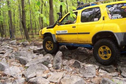 1991 Ford Bronco - Yellow SUV navigates a challenging rocky path through a wooded area.