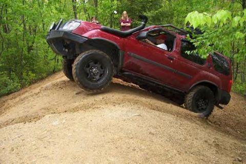 1991 Ford Bronco - Red SUV with snorkel and off-road tires climbing a dirt hill.