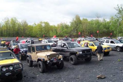 1991 Ford Bronco - Several off-road vehicles are parked together in an outdoor lot, with trees lining the horizon under a cloudy sky.