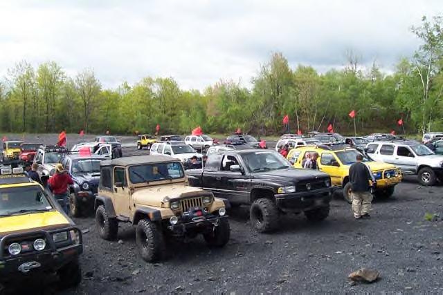 group of Jeeps and trucks parked on gravel lot with trees in background