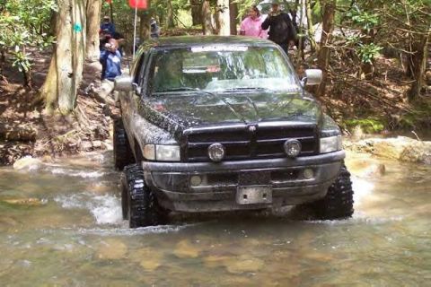 1991 Ford Bronco - A black pickup truck navigates through a rocky stream, kicking up water as it goes.
