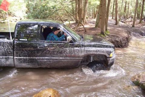 1991 Ford Bronco - Pickup truck navigates a water obstacle in a wooded area.