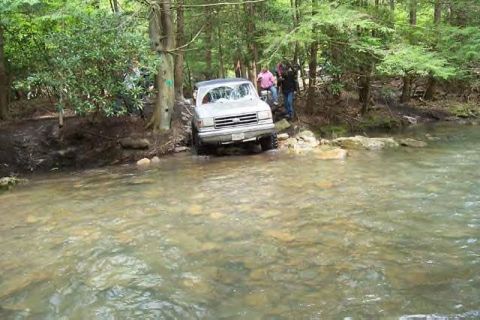 1991 Ford Bronco - A 1991 Ford Bronco navigates a rocky stream bed surrounded by trees.