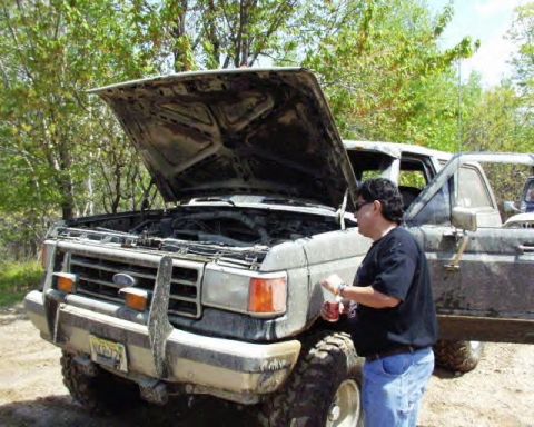 1991 Ford Bronco - Person checks engine of a muddy 1987 Ford F-Series truck with hood open.