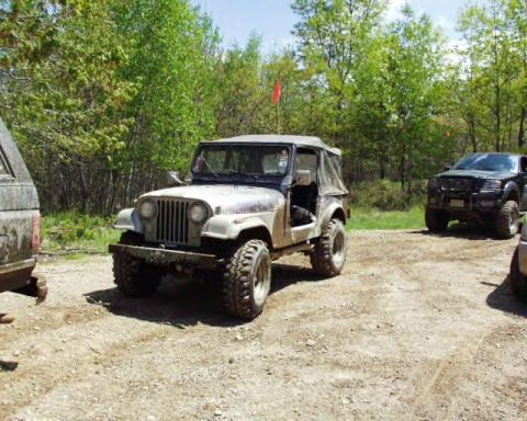 1991 Ford Bronco - A vintage Jeep CJ-5 is parked on a dirt path, with other vehicles visible in the background.