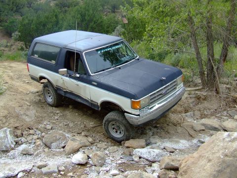 1987 Ford Bronco - This 1987 Ford Bronco navigates a rocky off-road path, demonstrating its capability on challenging terrain.