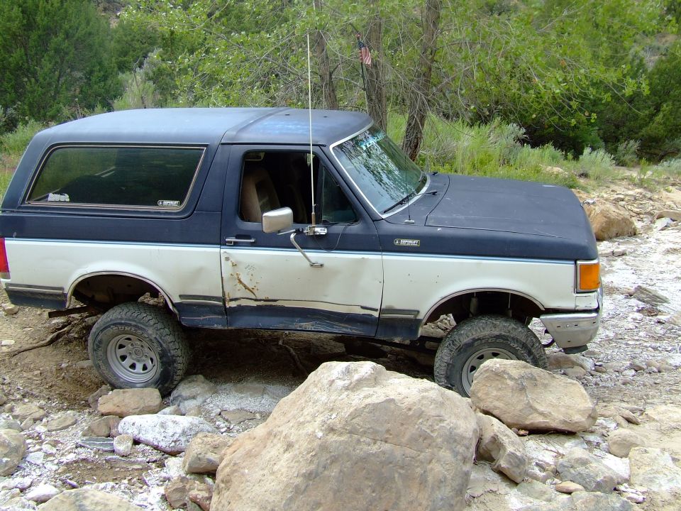 1987 Ford Bronco navigating a rocky trail, with damage to the driver's side door