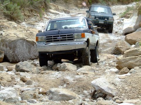 1987 Ford Bronco - Two SUVs navigate a challenging rocky terrain, with the lead vehicle being a Ford Bronco.