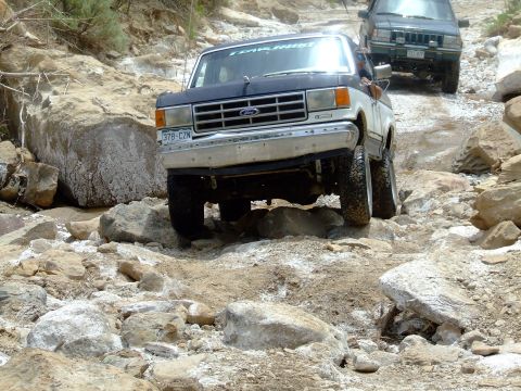 1987 Ford Bronco - A 1987 Ford Bronco navigates a challenging rocky terrain, with another SUV following behind.