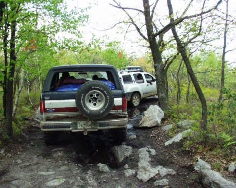 1991 Ford Bronco - A 1991 Ford Bronco navigates a challenging off-road trail, with another SUV visible in the background.