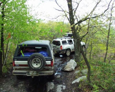 1991 Ford Bronco - Two SUVs navigate a challenging off-road path, with one Ford Bronco loaded for an adventure.