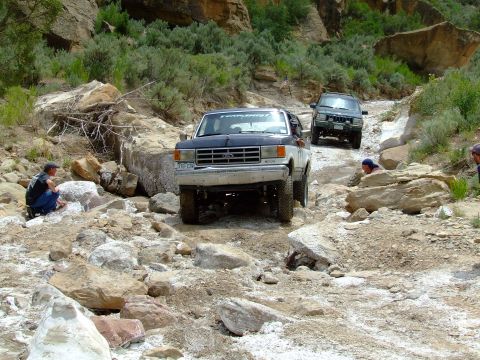 1987 Ford Bronco - A 1987 Ford Bronco navigates a challenging rocky terrain with another SUV following behind.