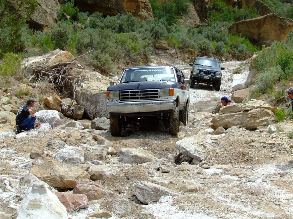Two-tone blue and white 1987 Ford Bronco driving on a rocky, off-road trail