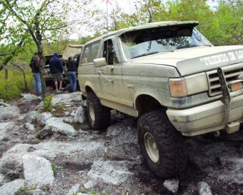 1991 Ford Bronco - A group of people are gathered around two off-road vehicles on a rocky, wooded trail.