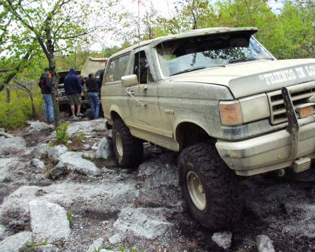 Muddy 1991 Ford Bronco on rocky terrain with people around another vehicle
