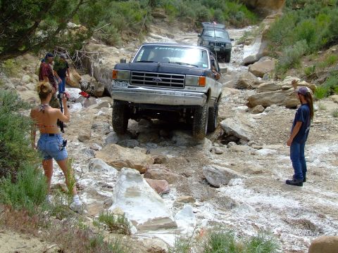 1987 Ford Bronco - A 1987 Ford Bronco navigates a challenging rocky terrain, with other vehicles and onlookers present.