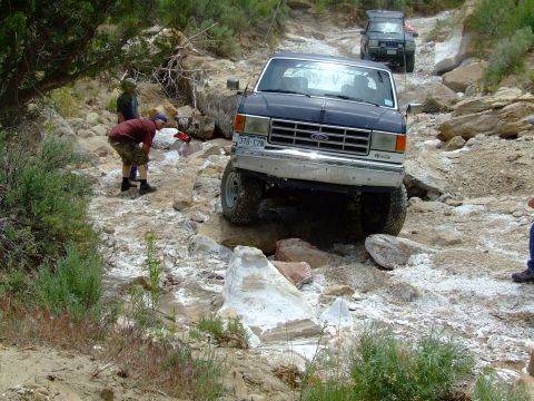 1987 Ford Bronco - A 1987 Ford Bronco tackles a challenging rocky off-road path, with another vehicle following behind.