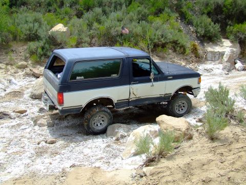 1987 Ford Bronco - This two-tone Ford Bronco navigates a challenging rocky trail, demonstrating its off-road capabilities.