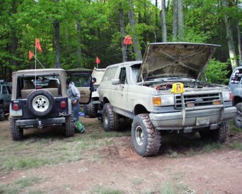 1991 Ford Bronco - A white 1991 Ford Bronco with its hood open is parked in a wooded area next to a Jeep and other vehicles.