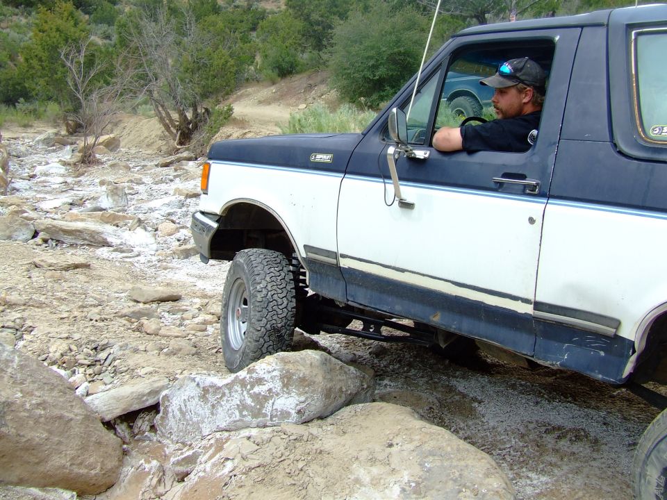 1987 Ford Bronco driving over rocky terrain, driver visible inside