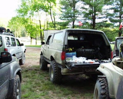1991 Ford Bronco - This 1991 Ford Bronco is seen with its tailgate open, revealing stored items, parked alongside other off-road vehicles.