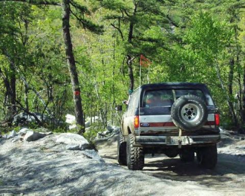 1991 Ford Bronco - A Ford Bronco navigates a rocky, wooded trail during the daytime.