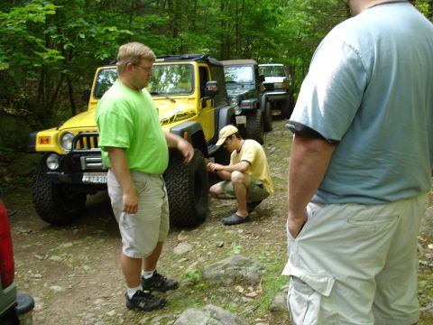 1996 Ford Bronco - Several Jeeps are lined up on a wooded trail, with people attending to one of the vehicles.