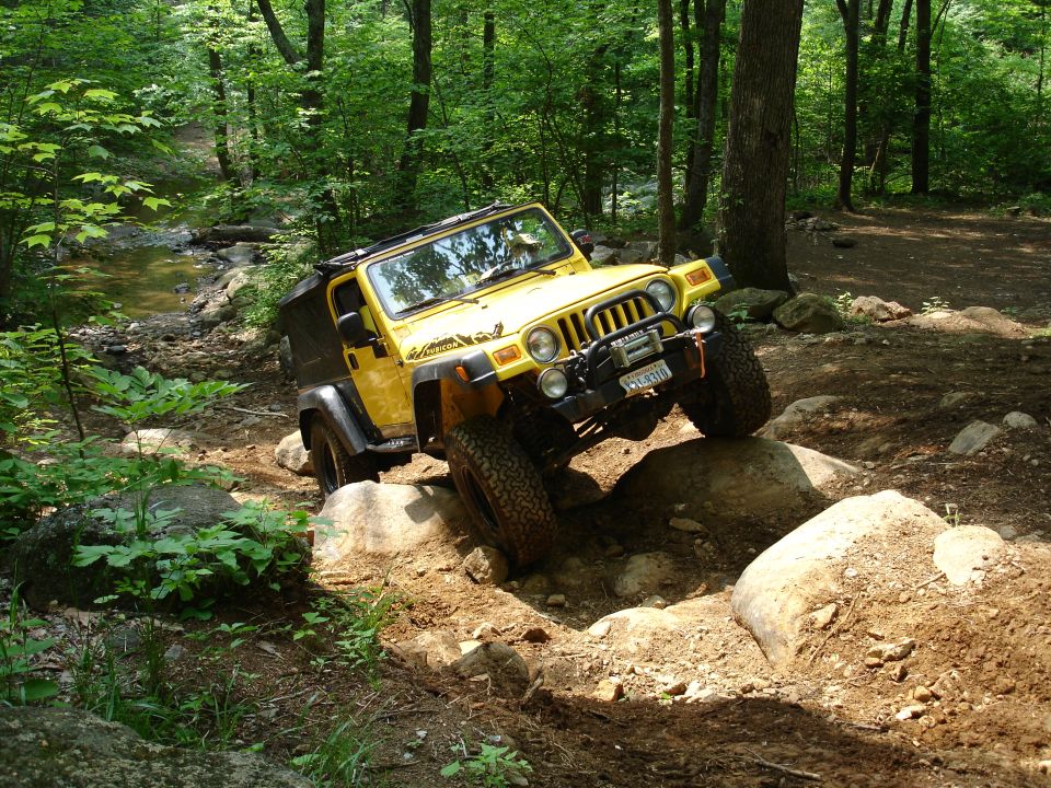 Yellow Jeep Wrangler navigating a rocky trail, front right tire on a large rock